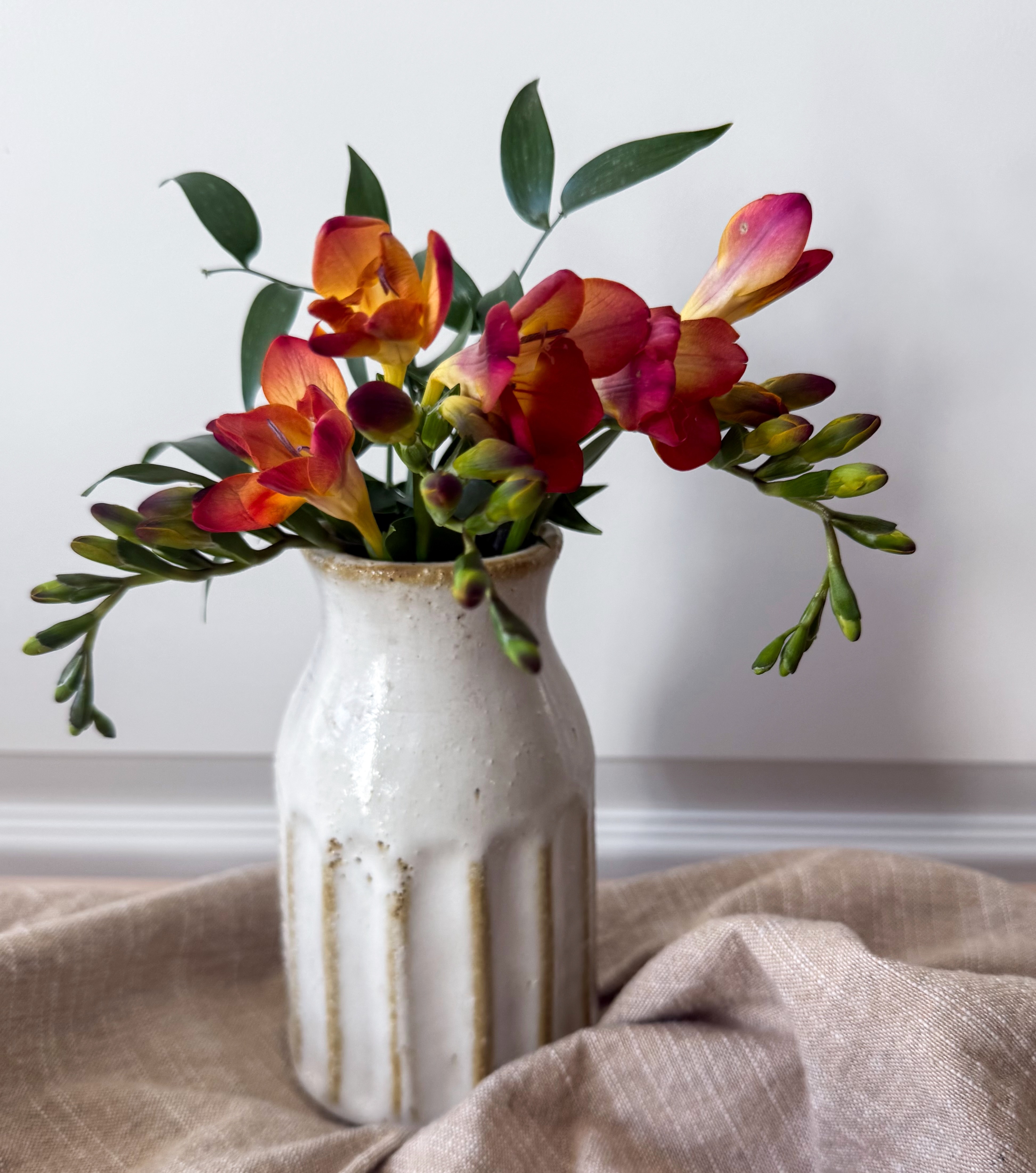 Orange freesia in white ribbed ceramic vase