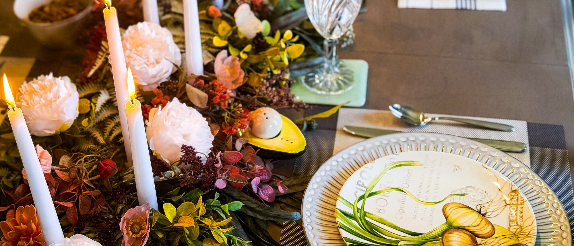 A long dinner table lit with white tapers, peonies and dahlias running down the centre, a botanical plate at each setting.