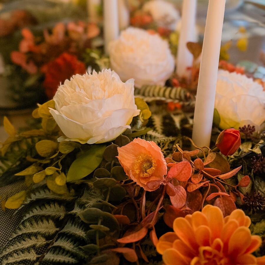 Lit taper candles rising from a runner of peonies, dahlias and autumn foliage.