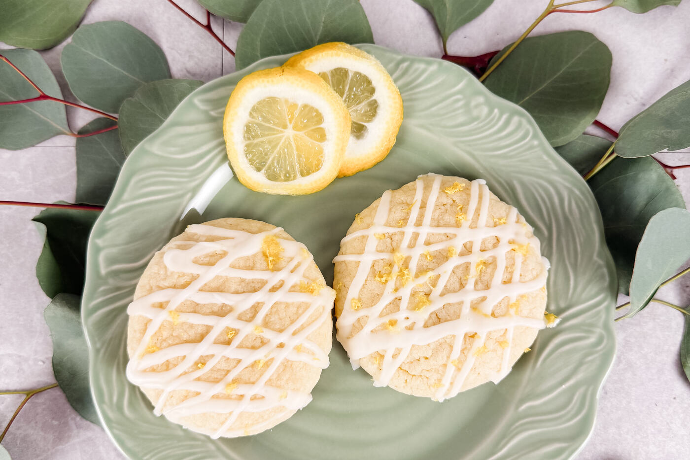 Iced lemon sugar cookies on a green plate with eucalyptus and lemon slices.
