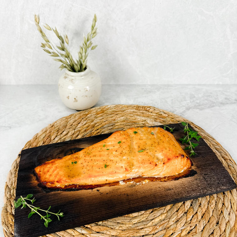 A roasted salmon fillet on a charred cedar plank set on a rope trivet.