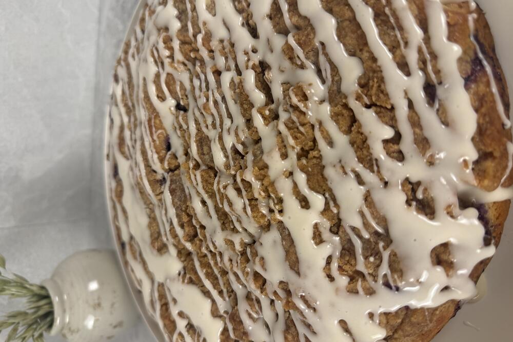 A blueberry crumb cake seen from above, glazed in white icing, cooling on parchment.