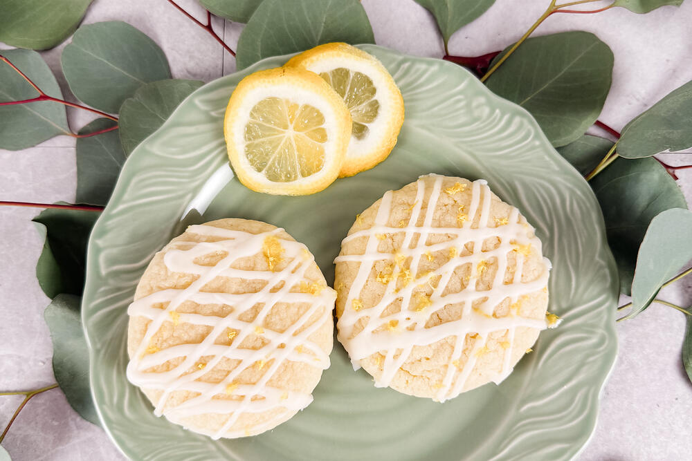 Iced lemon shortbread rounds on a green plate, surrounded by eucalyptus and lemon slices.