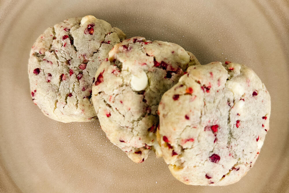 Three cranberry and white chocolate cookies on a warm tan plate.