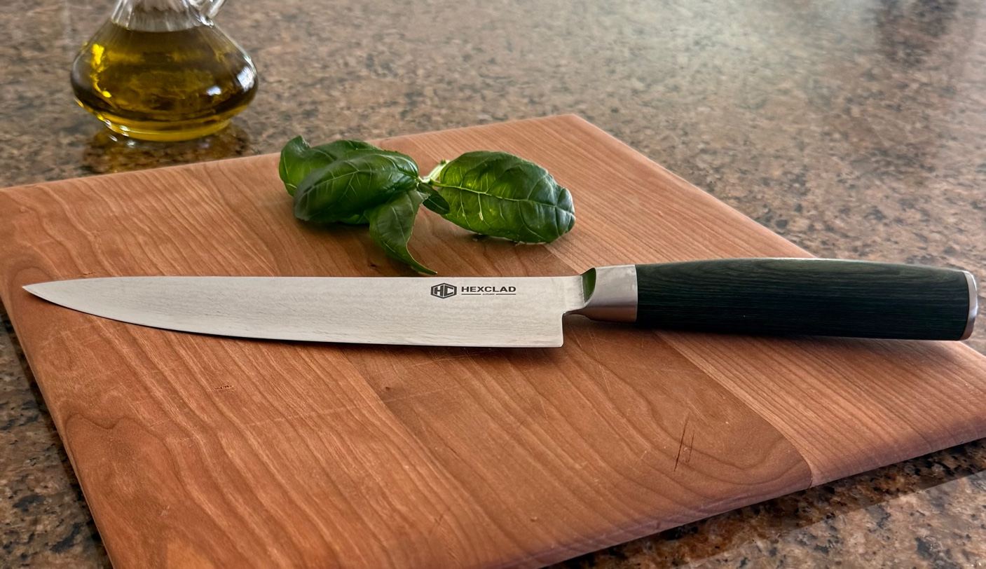 A chef's knife and fresh basil on a wooden cutting board.