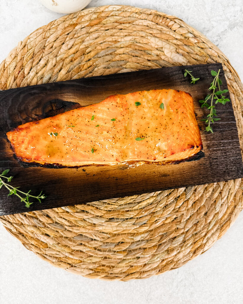 An overhead cedar plank of roasted salmon on a woven rope trivet.