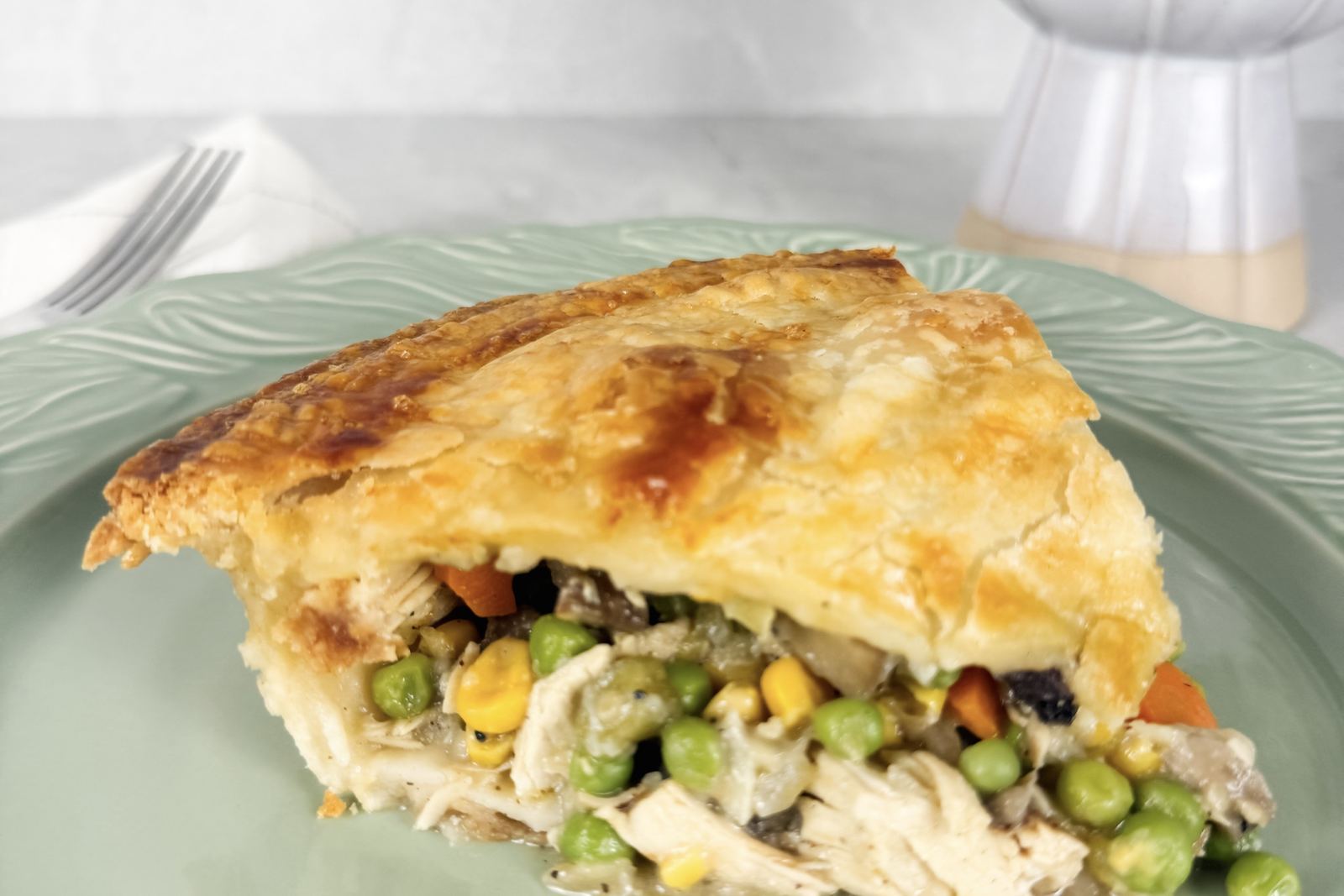 A golden double-crust chicken pot pie with a slice cut and served, the filling of chicken, peas and carrots showing.