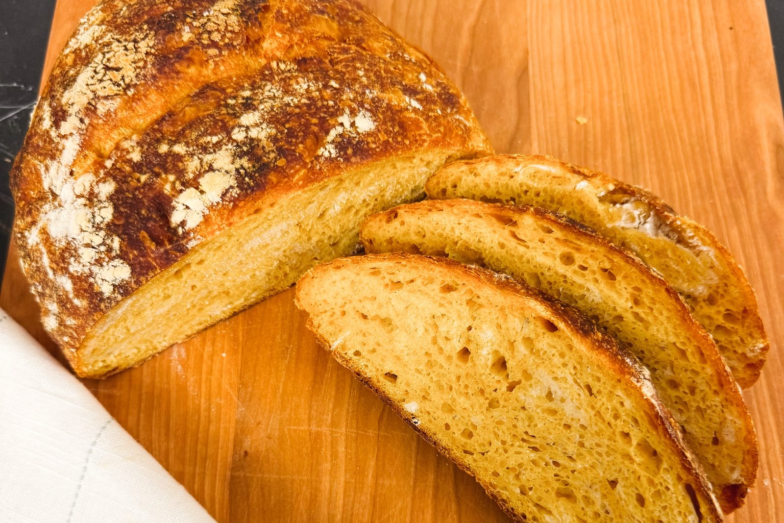 A pumpkin sourdough loaf on a cherry cutting board, three slices fanned out to show the golden crumb