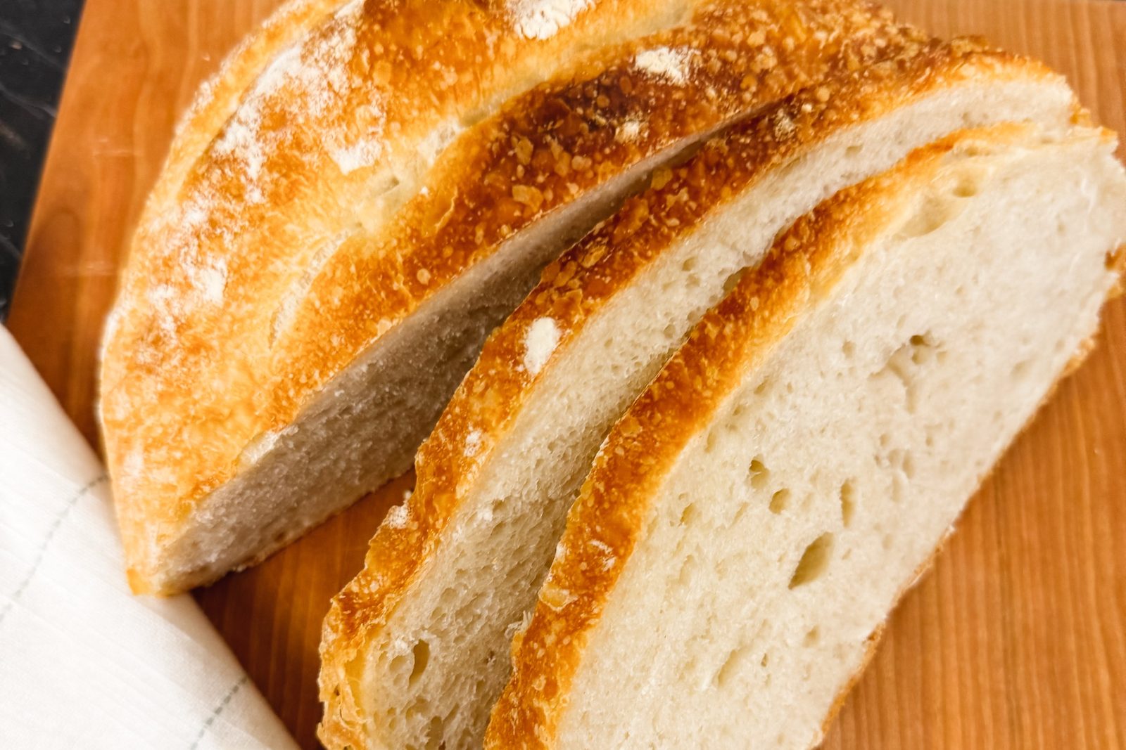 A sourdough loaf on a cherry cutting board, two slices cut to show the open white crumb