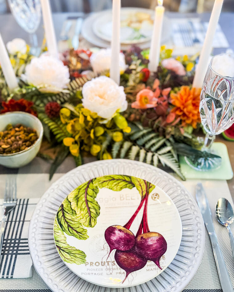 A single place setting with a botanical beet plate, striped napkin and candlelight.