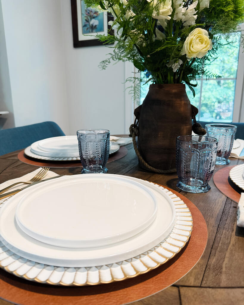 A close place setting with stacked white plates, gold flatware and smoke-grey pressed glass.