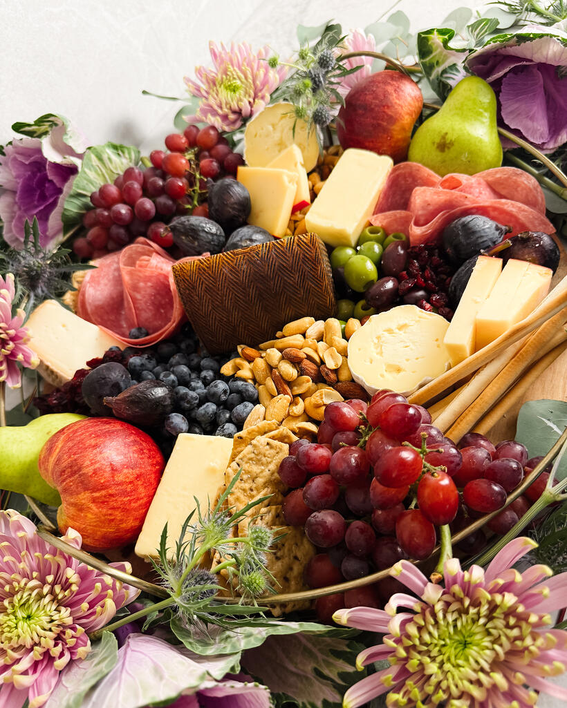 A grazing board of cheeses, cured meats, figs and grapes ringed with eucalyptus and chrysanthemum.