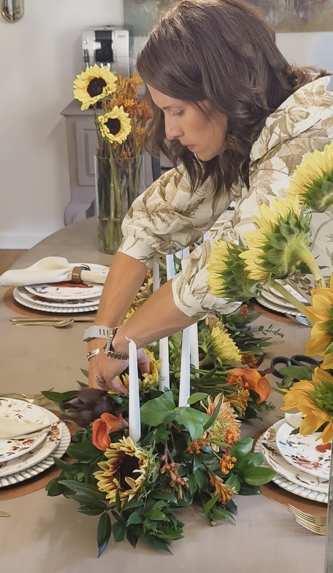 Setting white tapers into the sunflower runner on the long table, place settings with linen napkins on either side.